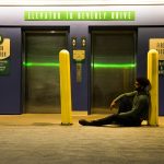 A man sitting by an elevator entrance under neon lights at night.