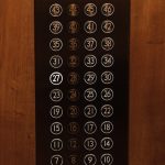 Close-up of a vintage elevator button panel with illuminated numbers in warm tones.